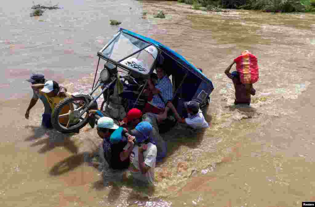 Residents carry a motorcycle taxi through a stream flooded by rains caused by the direct influence of Cyclone Yaku, in Piura, Peru, March 11, 2023.