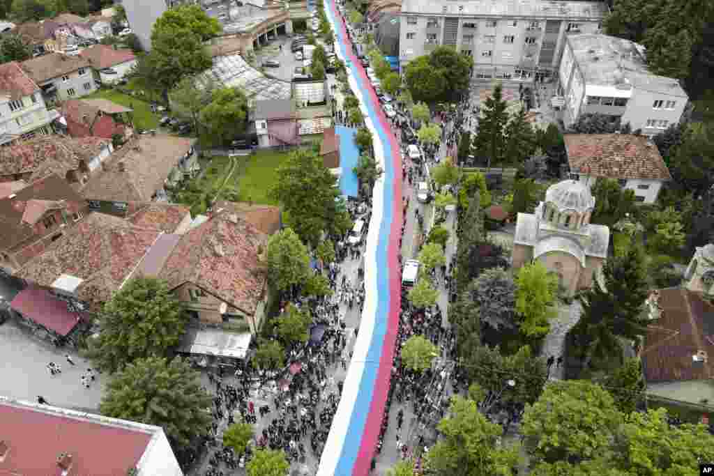 People hold a giant Serbian flag during a protest in the town of Zvecan, northern Kosovo. Hundreds of ethnic Serbs began gathering in front of the city hall in their repeated efforts to take over the offices of one of the municipalities where ethnic Albanian mayors took up their posts last week.