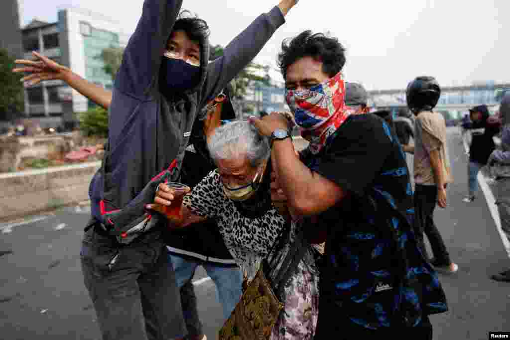 Demonstrators cover an elderly woman during clashes with police, as they protest against the government's proposed labor reforms in a controversial "jobs creation" bill in Jakarta, Indonesia.