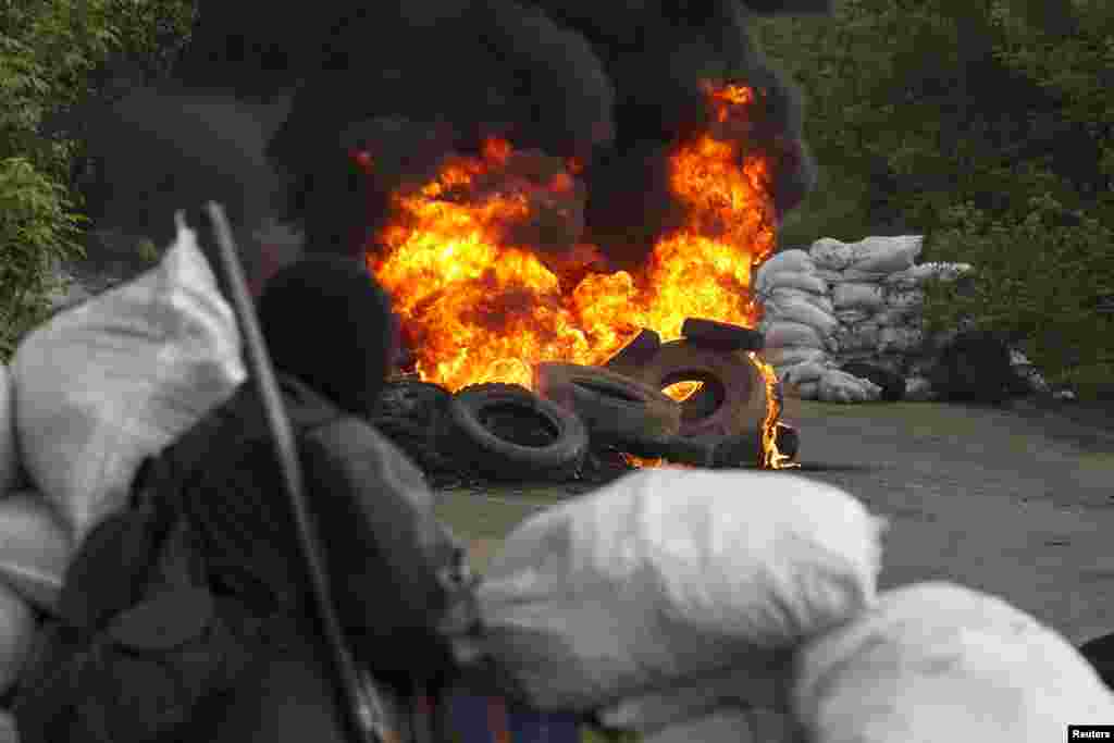 A pro-Russian separatist guards a checkpoint as tires burn in front of him, near the town of Slovyansk, Ukraine, May 2, 2014.