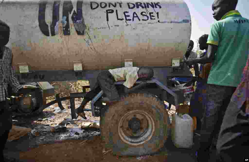 A young displaced boy rests on the wheel arch of a water truck while others fill containers from it, at a United Nations compound on the outskirts of Juba, the South Sudanese capital.