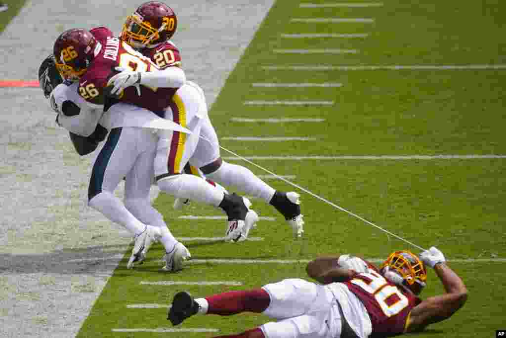 Washington Football Team defensive end Montez Sweat (90) falls while tearing a piece of of Philadelphia Eagles running back Jason Huntley's jersey who is being tackled by Washington Football Team strong safety Landon Collins (26) and cornerback Jimmy Moreland (20) during the first half of an NFL football game, Sept. 13, 2020, in Landover, Maryland. 