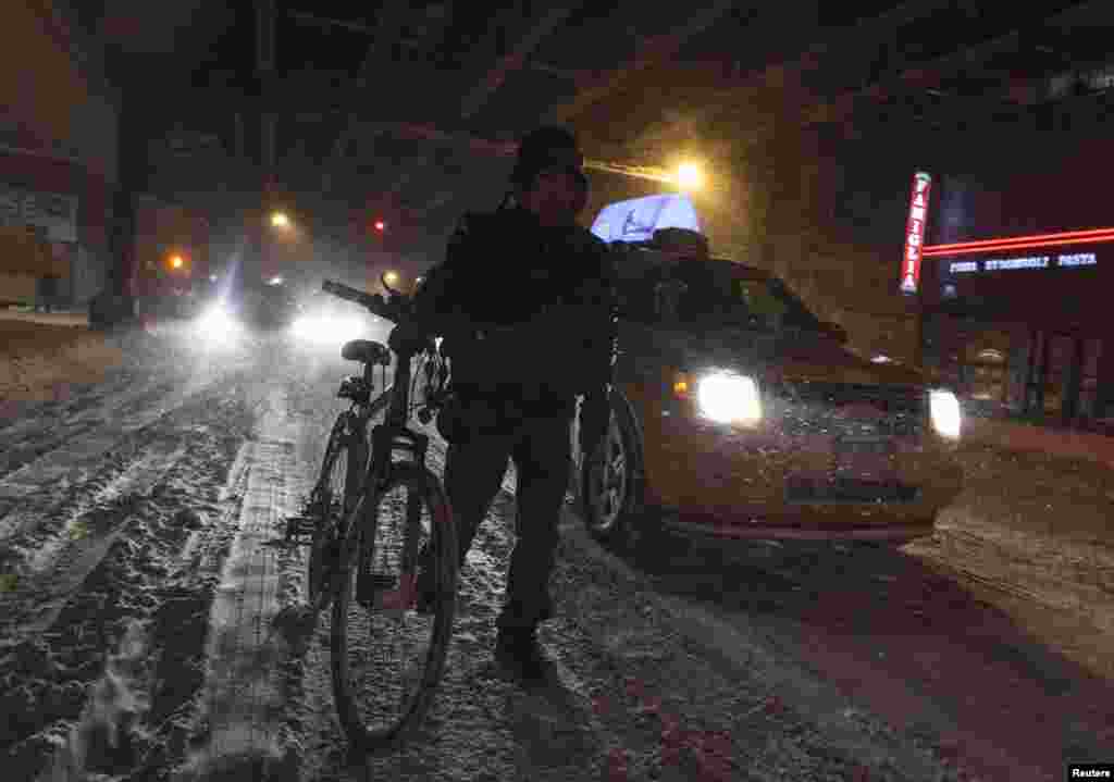 Phụ nữ dắt xe đạp đi qua đường phố trơn trượt vì bão tuyết ở New York, ngày 3/1/2014.