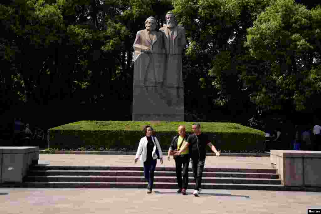 上海的一个公园里有共产主义理论家卡尔·马克思和弗里德里希·恩格斯的雕像。前面有三个人走过(2018年5月3日)。