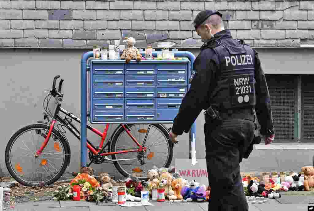 A police officer passes candles and teddy bears at the entrance of a house where five dead children were found in Solingen, Germany. The children's mother is suspected in the deaths.