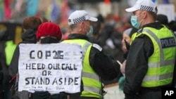 Una activista por el clima sostiene un cartel junto a policías cerca de la sede de la Conferencia de Naciones Unidas sobre Cambio Climático, o COP26, en Glasgow, Escocia, el 12 de noviembre de 2021. 