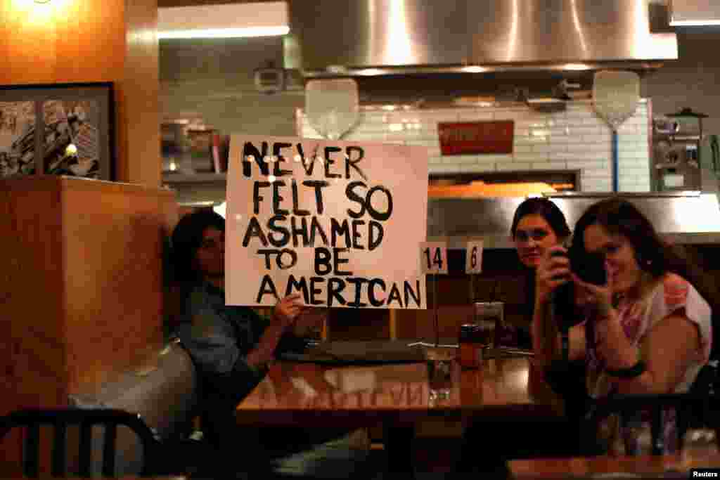 Patrons hold a sign as people march by while protesting the election of Republican Donald Trump as the president of the United States in downtown Los Angeles, California U.S., Nov. 9, 2016.