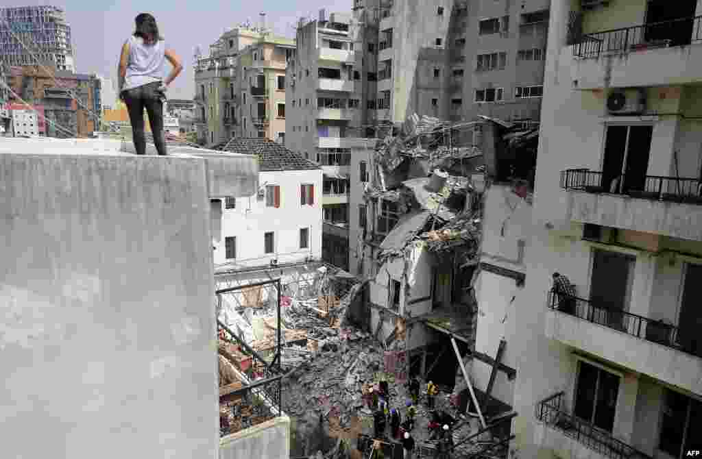 A woman looks on from a rooftop as rescue workers dig through the rubble of a badly damaged building in Lebanon's capital Beirut, in search of possible survivors from a mega-blast at the adjacent port one month ago, after scanners detected a pulse.