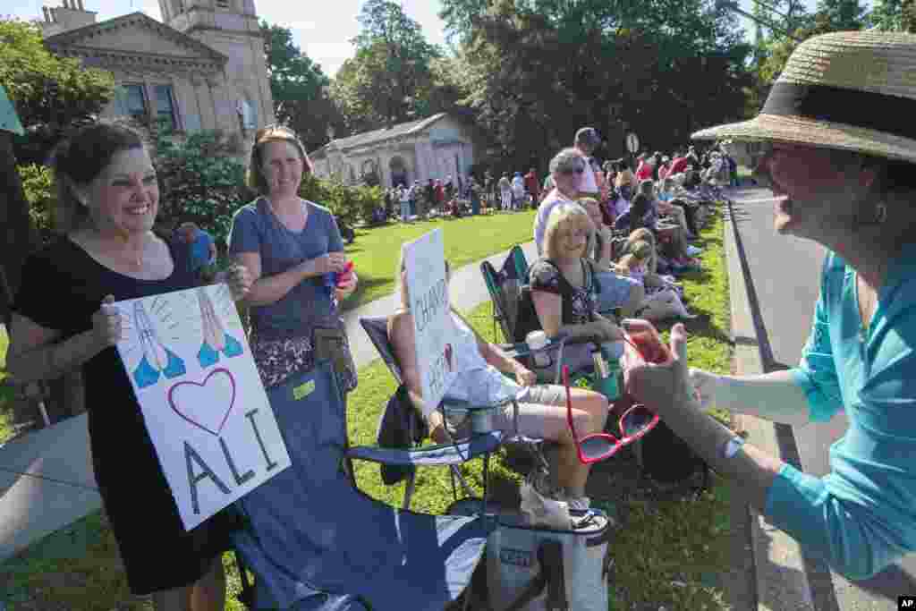 Cathy Gutgsell, left, holds a sign as she is photographed while spectators wait for the arrival of Muhammad Ali's funeral procession to enter Cave Hill Cemetery, Friday, June 10, 2016, in Louisville, Kentucky.