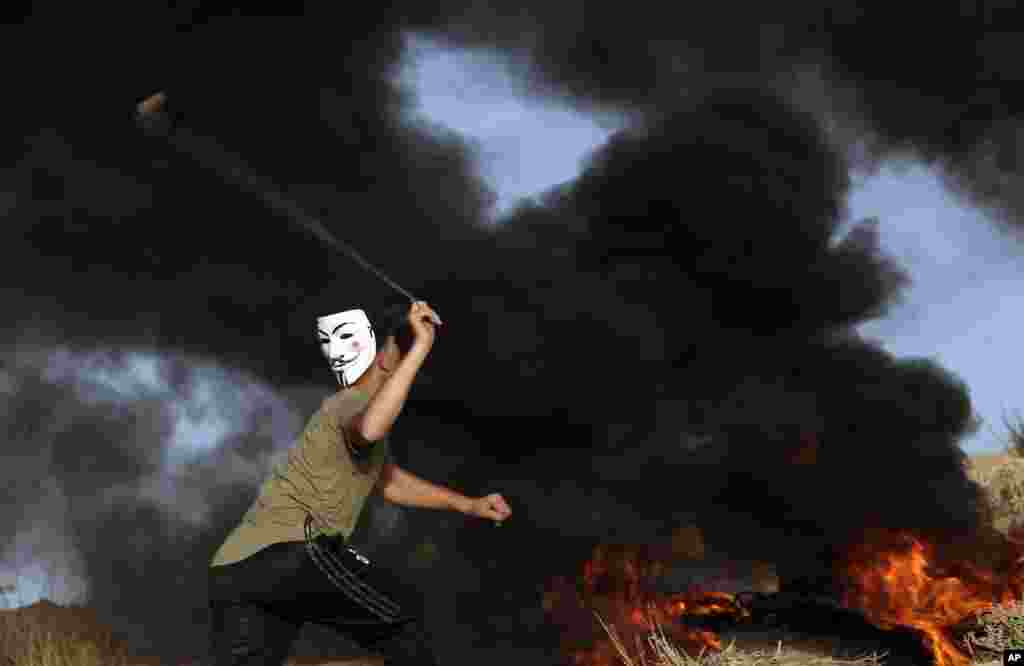 A protester hurls stones at Israeli troops while others burn tires near the fence of the Gaza Strip border with Israel during a protest on the beach near Beit Lahiya, northern Gaza Strip.