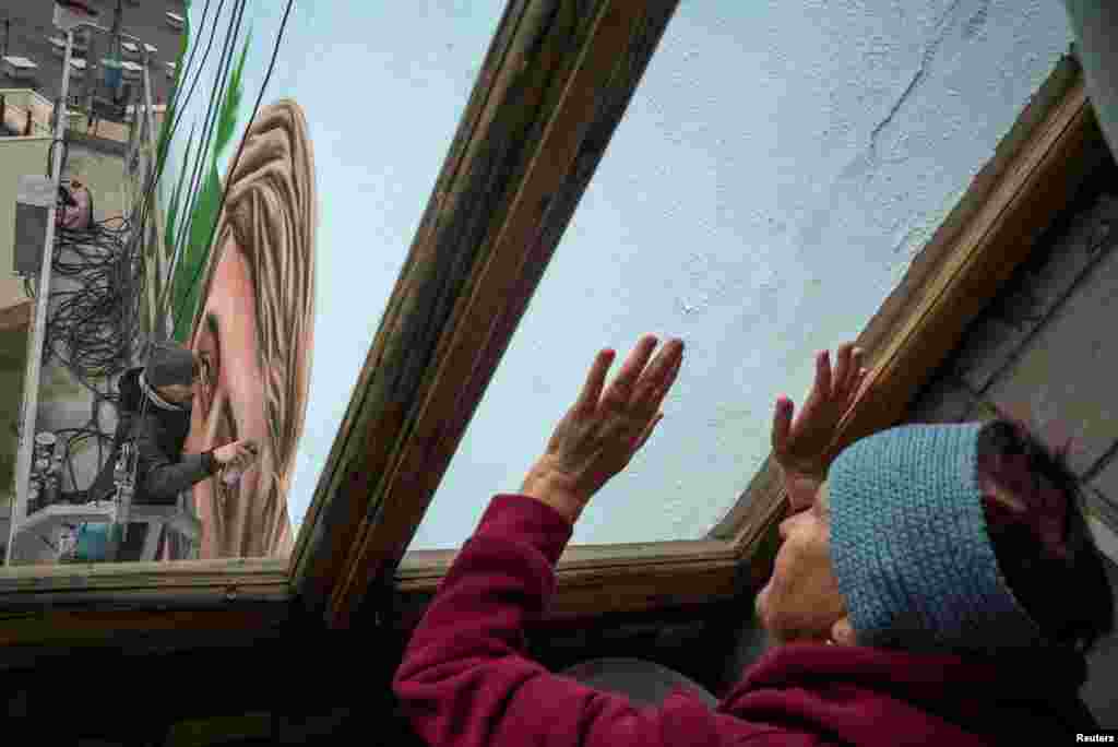 Tamara Bordus observa mientras el artista callejero, Eugene Gladenko, pinta un mural de su nieto, en la fachada de la casa donde solía vivir Maksym, en Kiev, Ucrania, el 18 de octubre de 2024. 