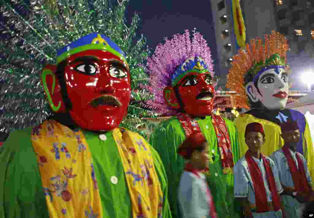 Indonesian youths stand near traditional giant effigies called "ondel-ondel" during a mass wedding held in celebration of the New Year in Jakarta, Indonesia, Sunday, Dec. 31, 2017. (AP Photo/Dita Alangkara)