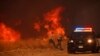 Policías del condado vuelven a su vehículo tras observar las llamas provocadas por el incendio Hughes junto a una carretera en Castaic, California, el 22 de enero de 2025.